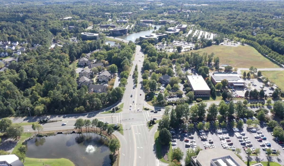 Aerial view: suburb with roads, buildings, pond, and trees.